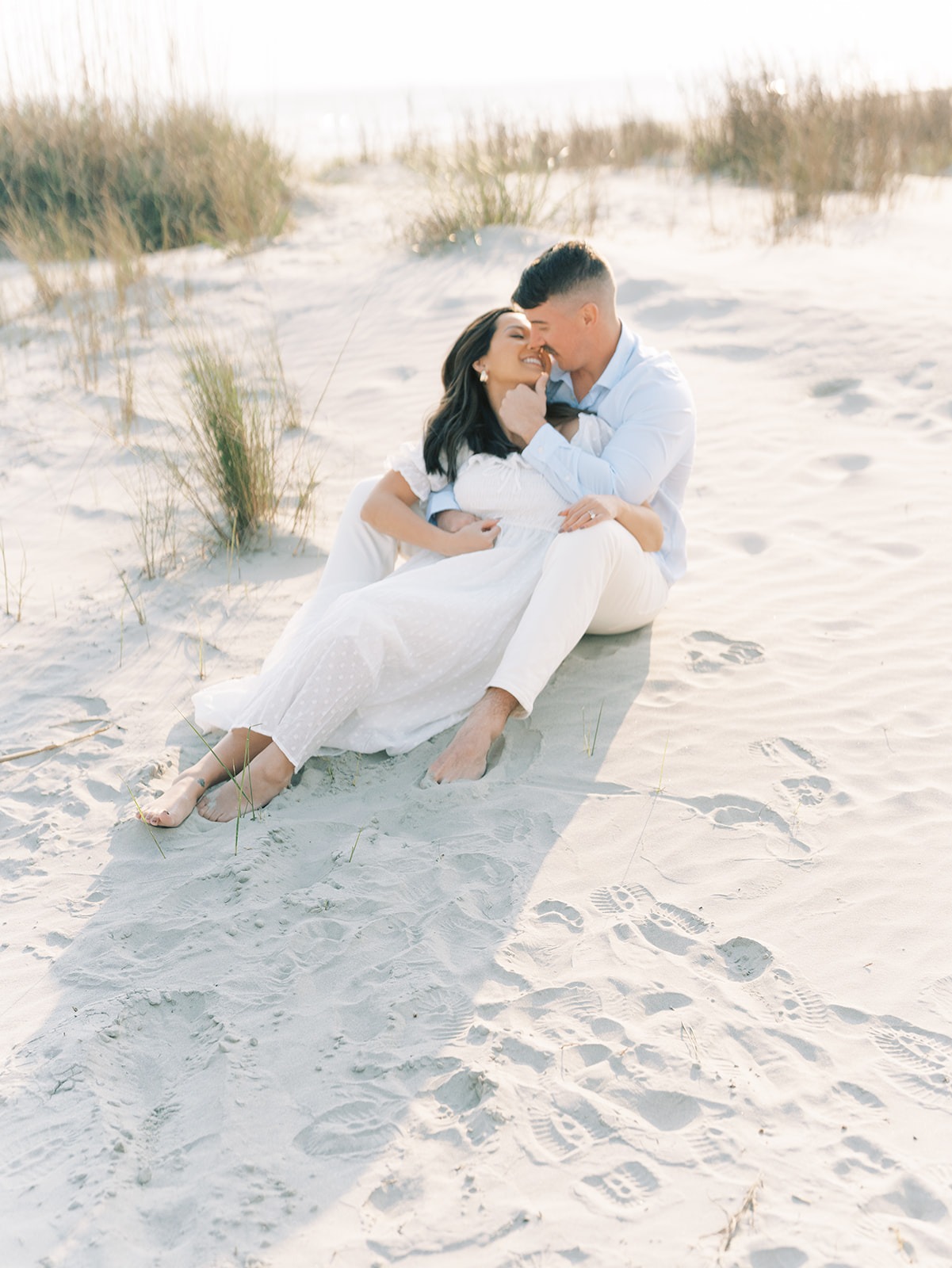 couple embracing while sitting in the sand at Isle of Palm during their engagement session